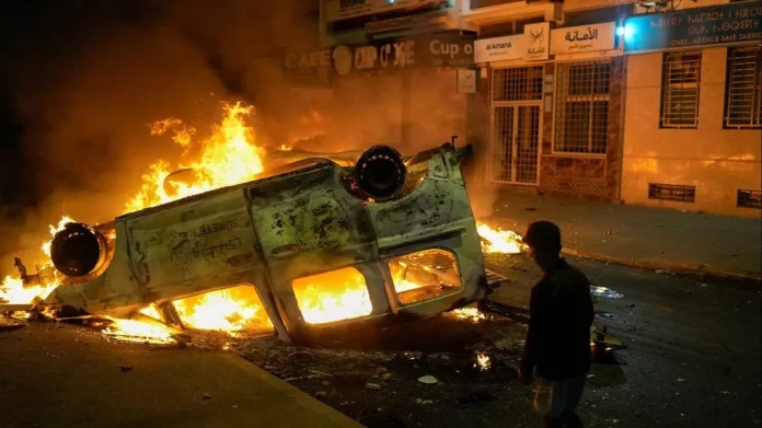 Un garçon se tient à côté d'un véhicule de police incendié, pendant les manifestations menées par des jeunes, Salé, au Maroc